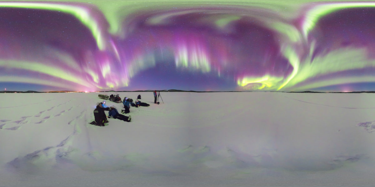 The tourist enjoying the northerh lighs in a icy lake. Inari. Finland
